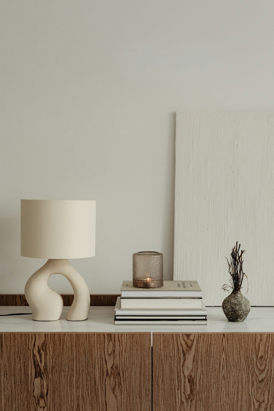 A sculptural ceramic lamp with a linen shade on a walnut sideboard