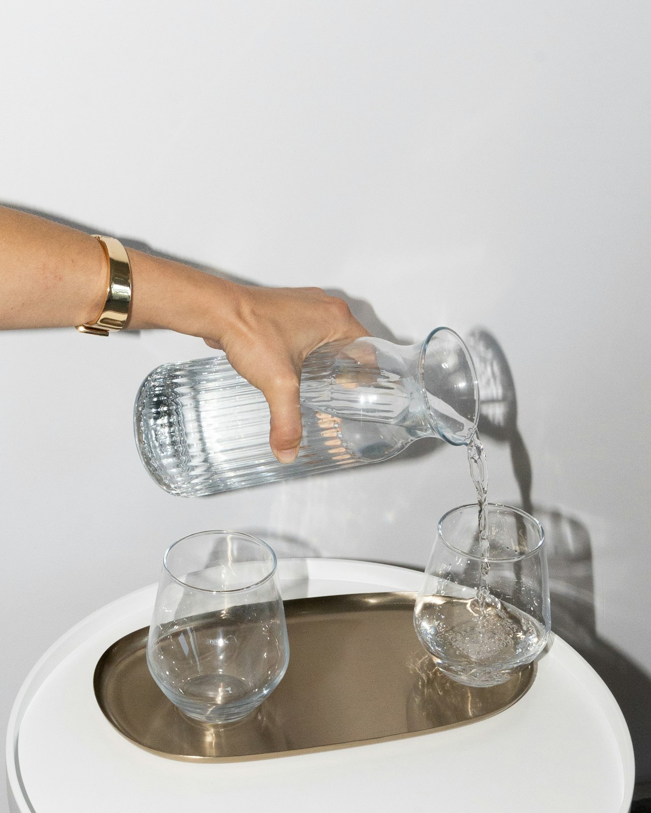 A hand pouring water from a ribbed glass carafe into tumblers