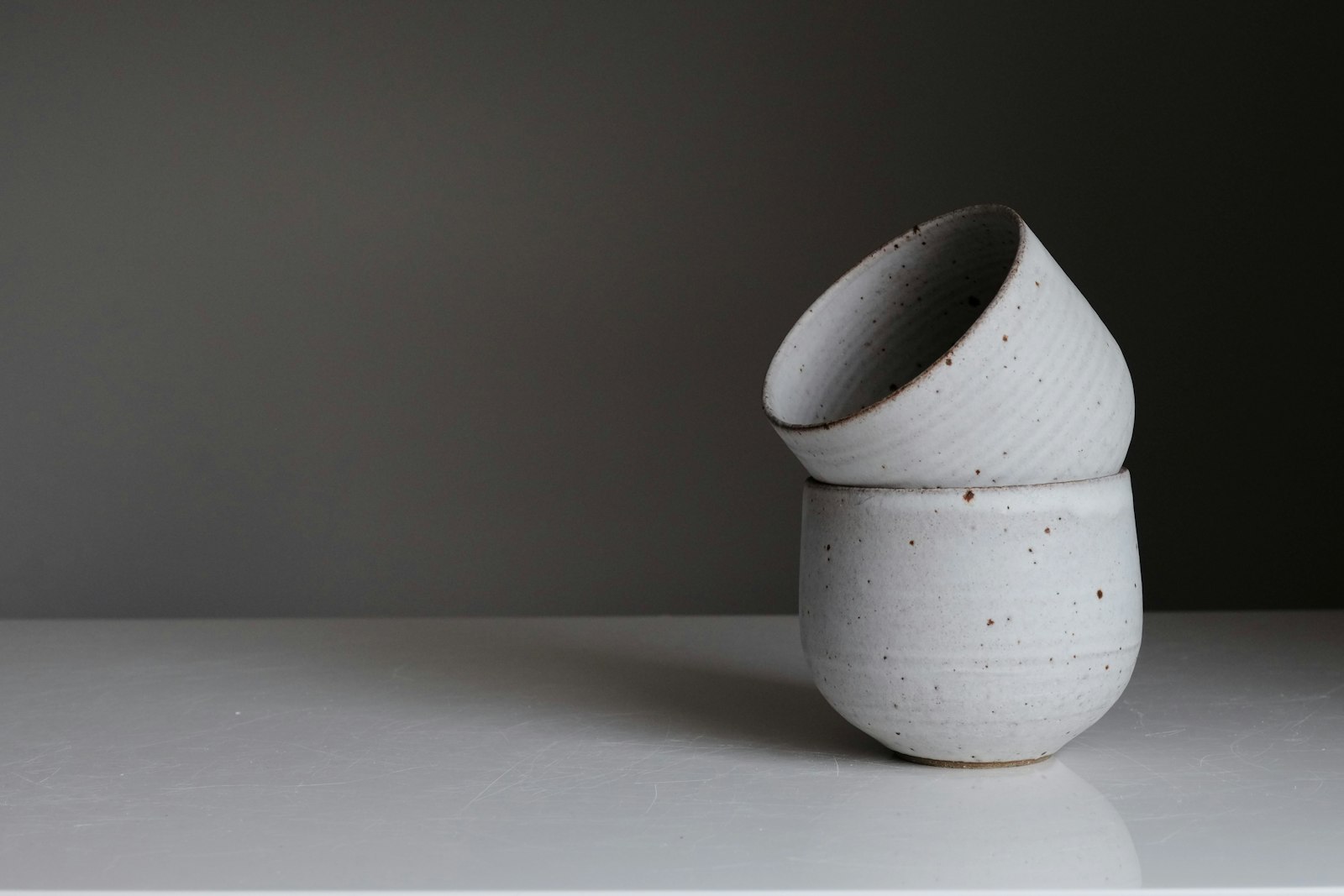 Two stacked speckled ceramic bowls against a dark wall