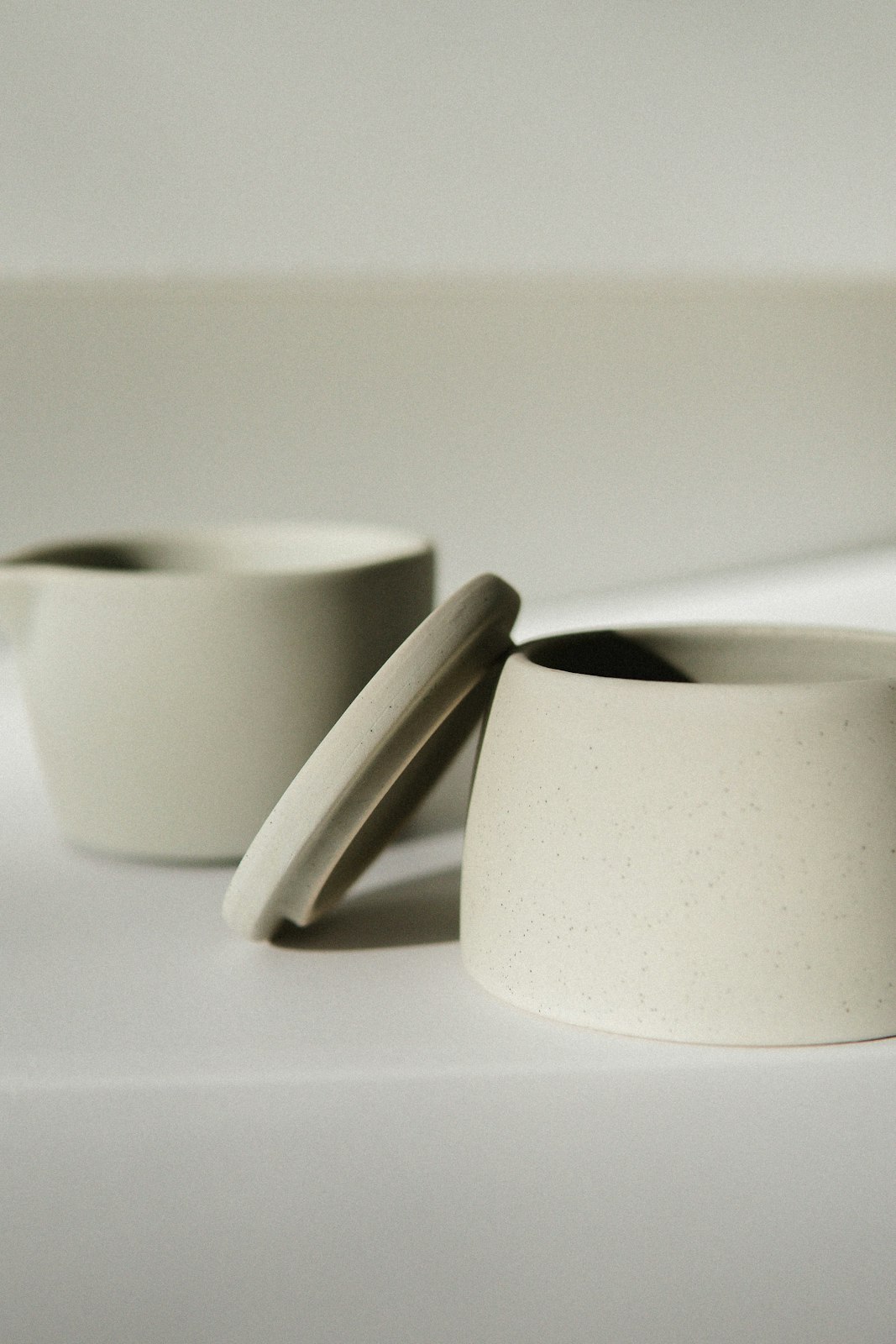 Two speckled stoneware cups with a lid on a pale table