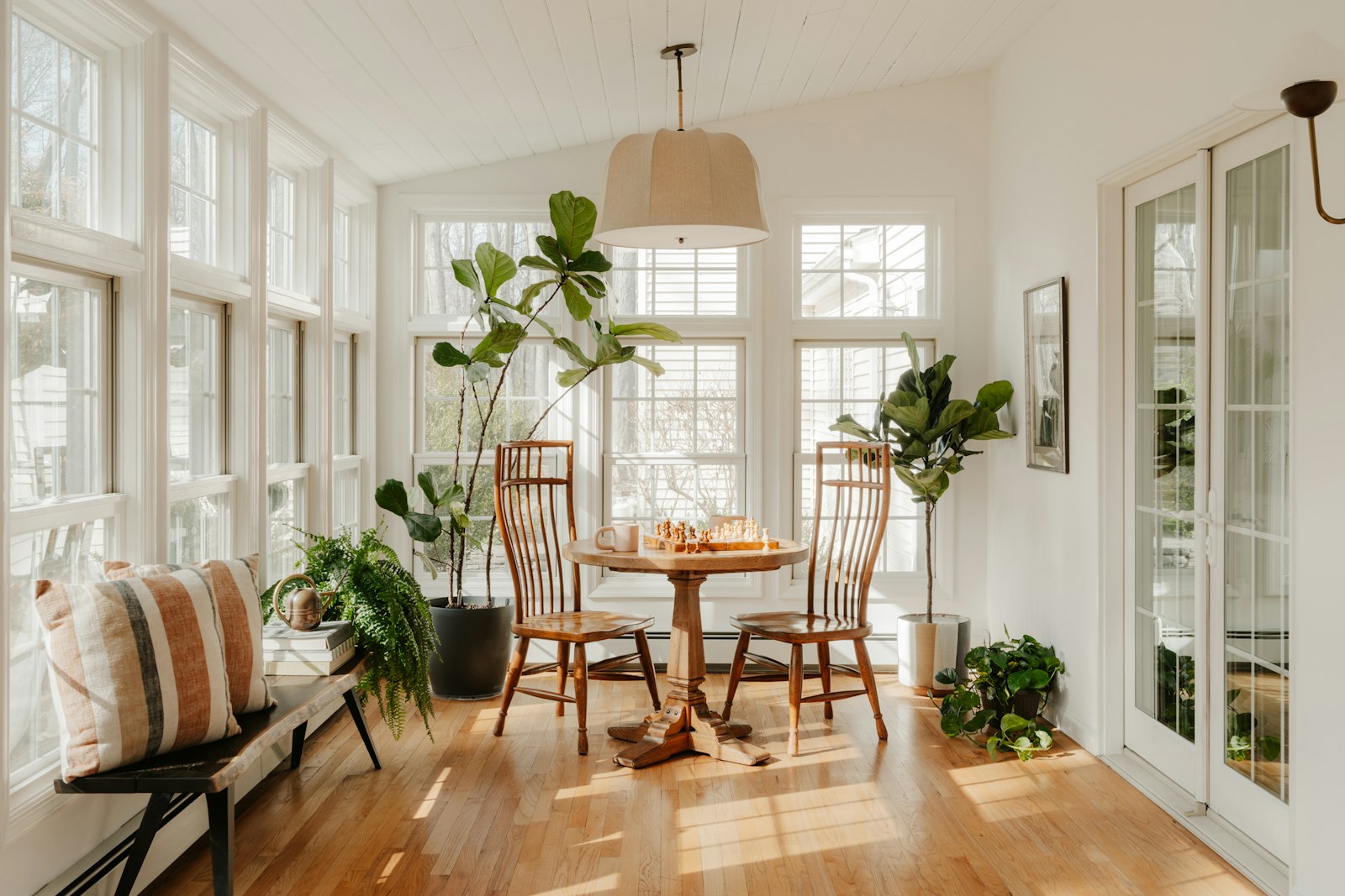 A sunroom with a round dining table, plants, and windows on three sides