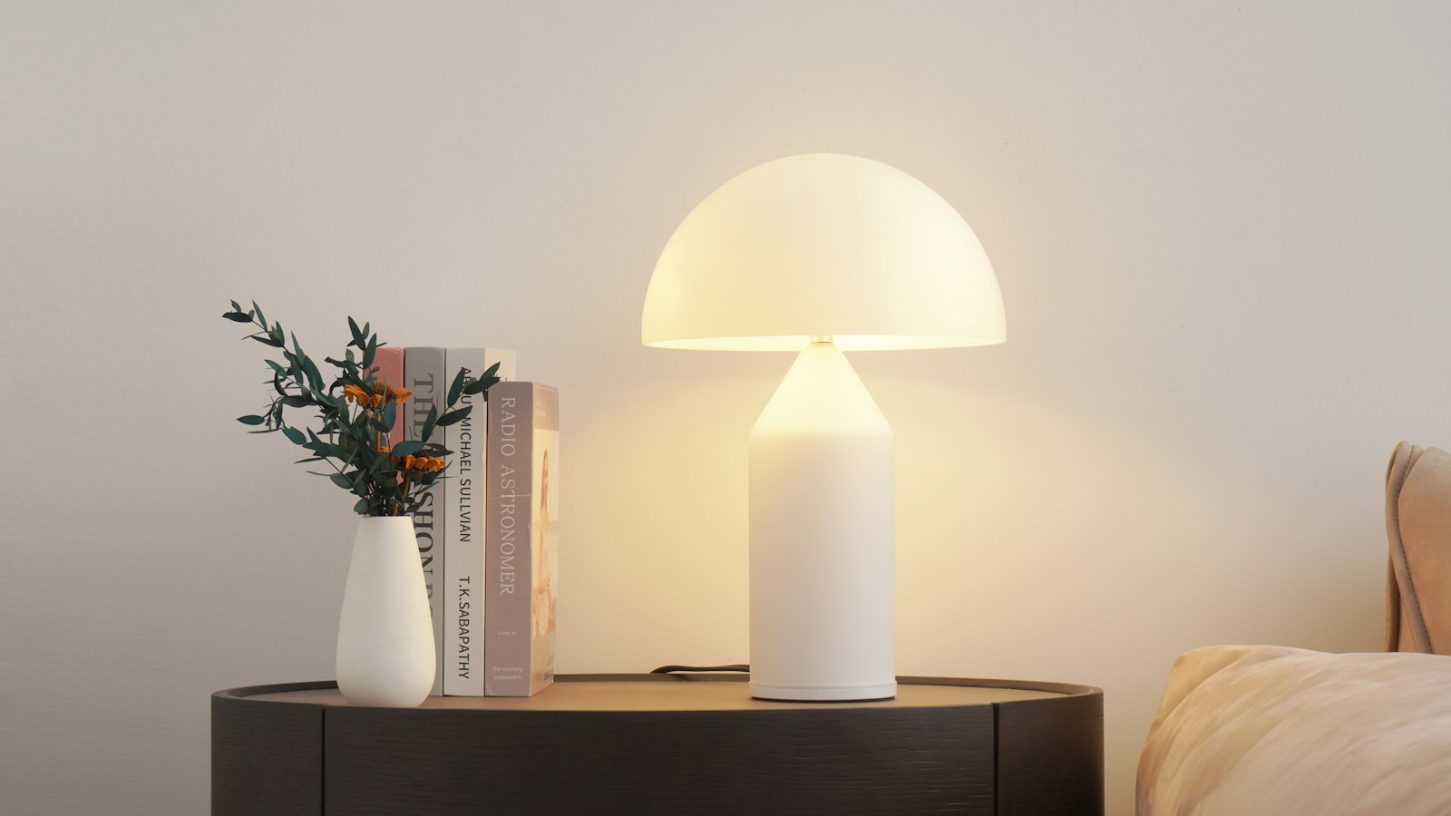 A white mushroom table lamp glowing beside books and a small vase