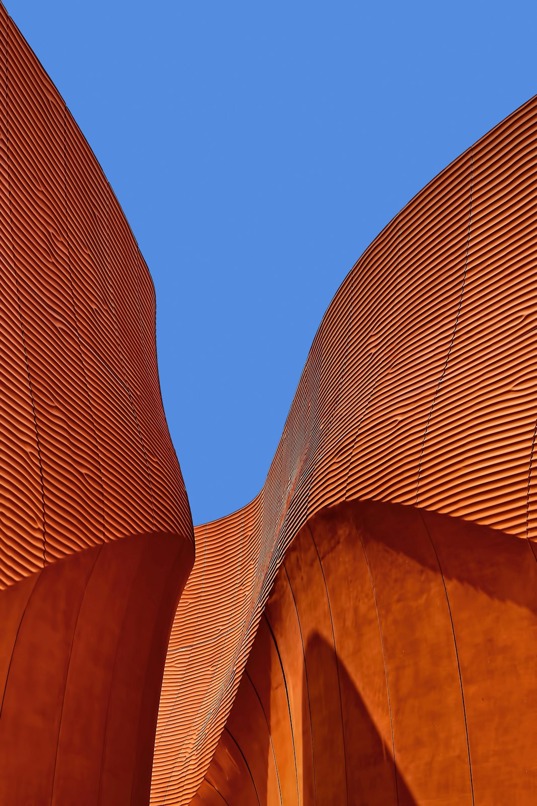 Wavy terracotta walls rising toward a blue sky
