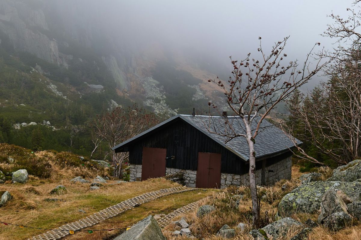 A dark wooden hut in fog on a rocky mountainside