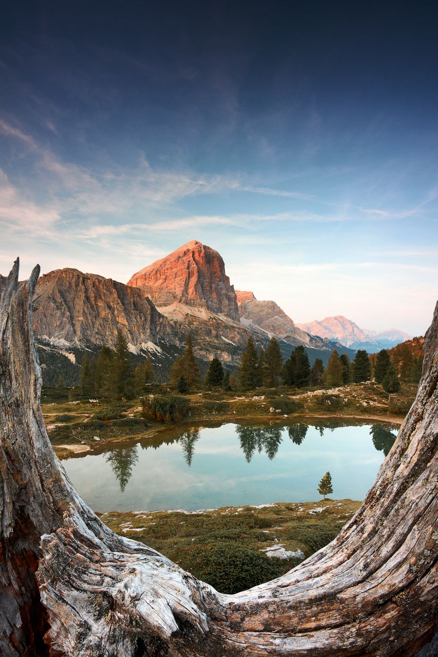 A small alpine lake below a peak lit by sunset, framed by weathered wood